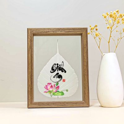 Pink lotus and Bình An calligraphy printed on a Bodhi leaf in a desk frame